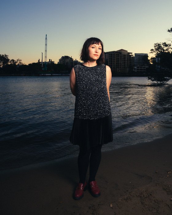 Leah Kardos standing on the riverbank at dusk in a sequinned dress, 2024